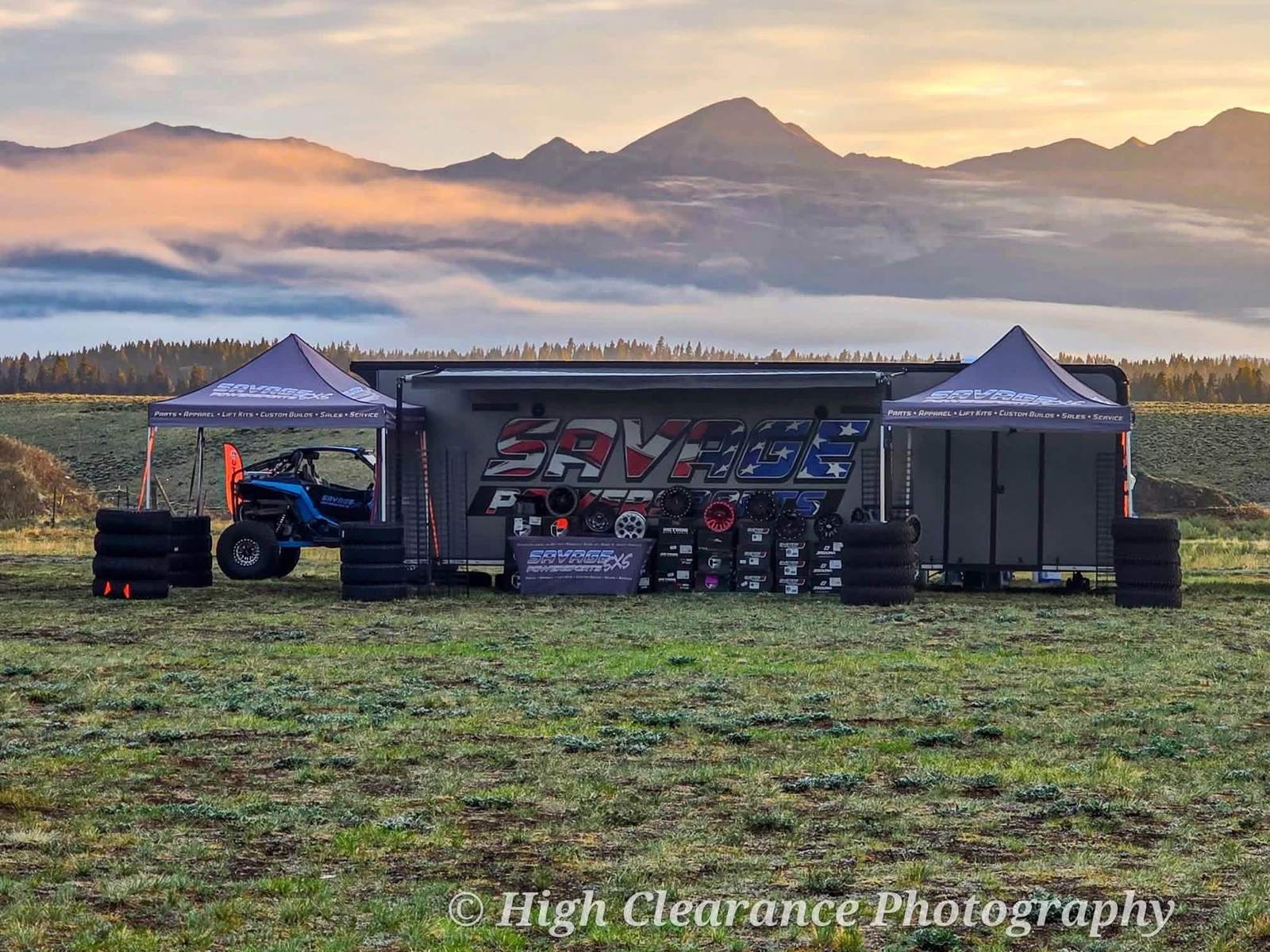 The Savage Powersports trailer and tents at sunrise at the Taylor Park UTV Rally, mountains and low cloud behind